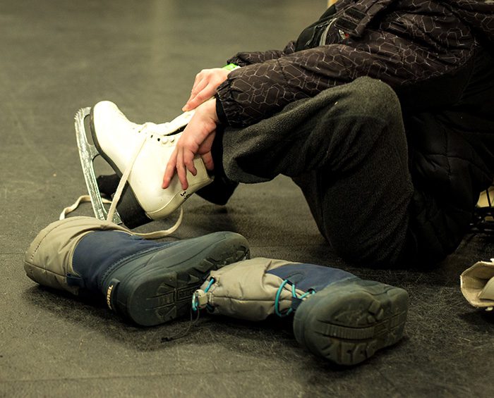 A young child's snowboots are tossed aside as they put on an ice skate.
