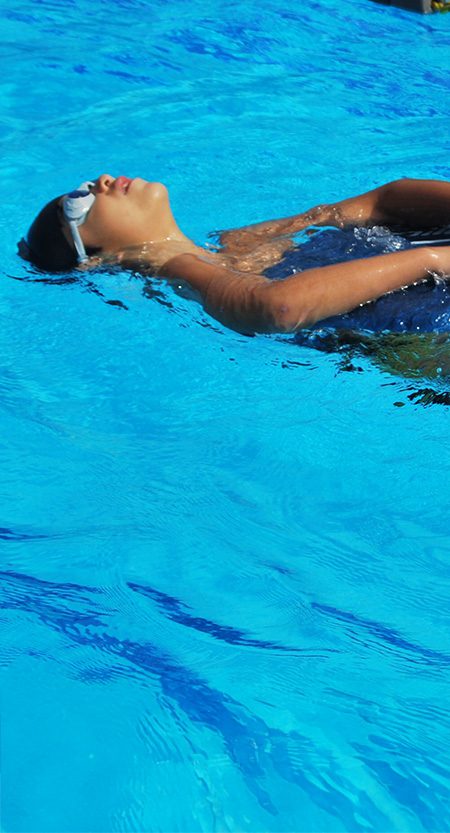A child floats on their back in a swimming pool.