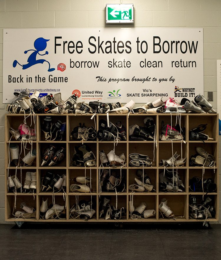 A large cubby system is overflowing with ice sates. A large sign above it reads, "Free Skates to Borrow".